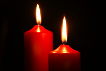 Zwei brennende rote Weihnachtskerzen vor schwarzem Hintergrund – festliche Atmosphäre und stimmungsvolle Beleuchtung