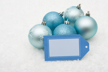Blue glass Christmas balls with blank gift tag on snow