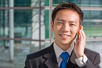 Good looking asian business man standing with mobile phone.