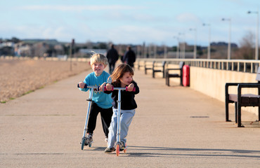 Young brother and sister scooting along a beach