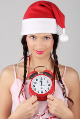 Beautiful christmas girl in santa hat with red alarm clock