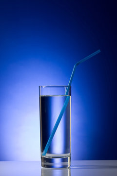 Glass with pure water with blue straw  on a blue background