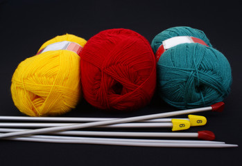 three woolen skeins and knitting needle on black background