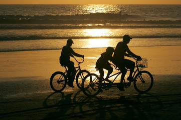 Fototapeta na wymiar Rodzina jazdy rowerami wzdłuż plaży o zachodzie słońca.