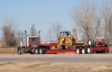 Semi-truck pulling a loaded drop-deck trailer.