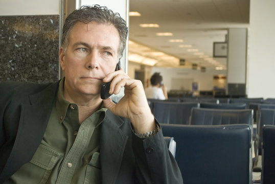 A man sitting in an airport talking on a cell phone.