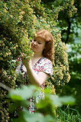 The brown-haired woman smells a blossoming bush