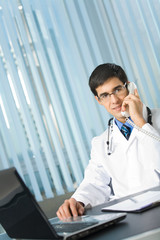 Portrait of happy successful doctor on phone at office