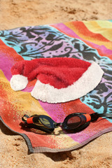 sandy beach with goggles, towel and santa christmas hat