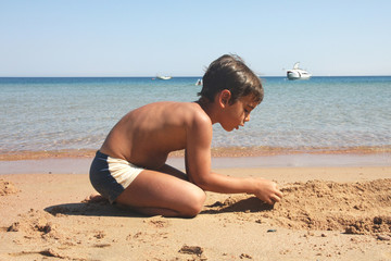 Boy constructing a pieces of sand on the beach. Summer.