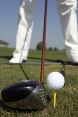 Head of golf club driver is aligned next to golf ball on tee