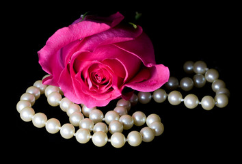 Bright pink rose and string of pearls on a black background