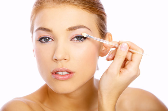 Portrait of beautiful blond woman doing makeup, on white