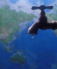 water faucet with one drop of water over a world map