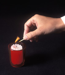a woman's hand lighting a red votive candle