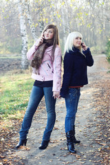 Two friends speaking on mobile phones outdoors in autumn