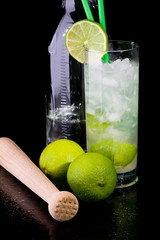 Caipirinha mit Limetten, Flasche und Stoessel auf schwarz