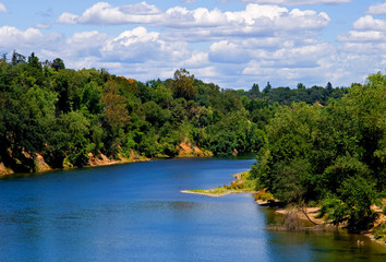 Fototapeta na wymiar ots of white clouds over a clean blue river with lots of trees