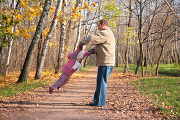 Fototapeta premium Grandfather rotates granddaughter in wood in autumn