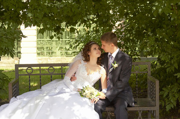 Groom and bride in the garden, sitting on the bench