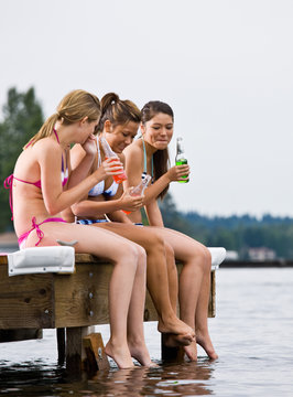 Friends Sitting On Pier At Lake Drinking Soda