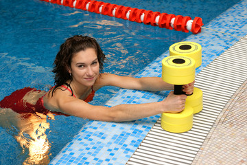 The girl is engaged aqua aerobics with dumbbells