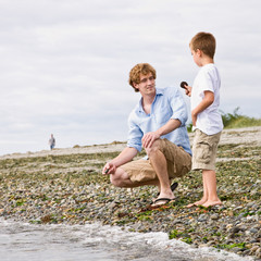 Fototapeta premium Father and son gathering rocks at beach