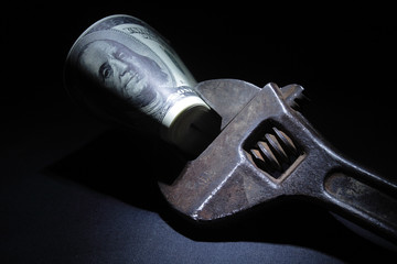 Rusty  spanner with dollar's bundle on dark background