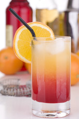 tequila Sunrise mit Strohhalm vor Flaschen und Früchten