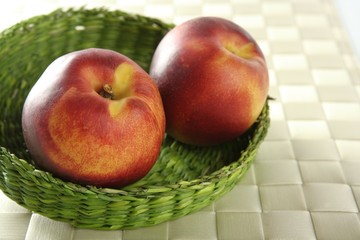 Two red peaches in a green basket