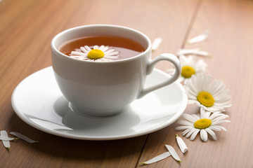 white cup of herbal tea and camomile flowers