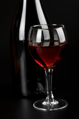glass of red wine and bottle over black background