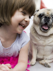 Adorale child smiling playing with her pet pug dog