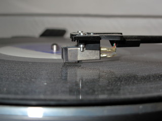 Tête de lecture sur disque vynil noir poussiéreux.