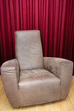 Big brown leather chair on wooden floor - red velvet curtain