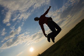 silhouette of a teenager jumping against blue sky at sunset