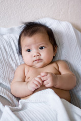 Baby lying in bed under blanket, hands together