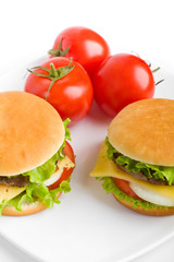 two cheeseburgers on a square plate with three ripe tomatoes