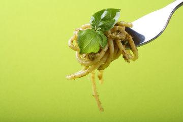 Italian pasta with pesto sauce and parmesan on fork.