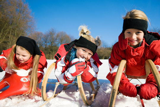 Drei Kinder fahren Schlitten im Schnee