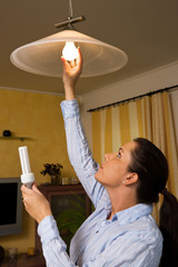 Young woman changes in energy-saving light bulb lamp