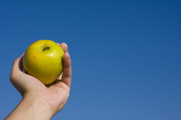 apple in girl's hand over blue sky