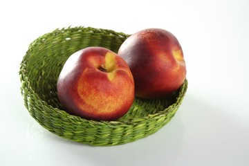 Two red peaches in a green basket