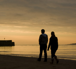 Silhouette of young couple walking on beach at sunset
