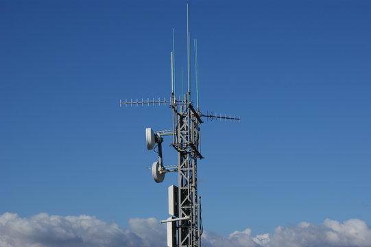 pitze eines Funkmastes mit mehreren Antennen vor blauem Himmel &ndash; moderne Kommunikationstechnik im urbanen Umfeld