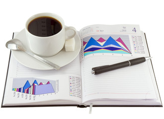 Coffee cup, pen, on the open organizer, financial diagrams.