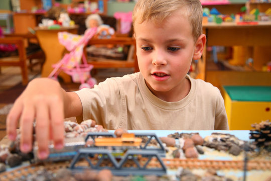 Boy plays with toy railroad in playroom
