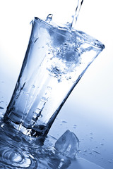 water splashing into glass with ice cubes