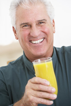 Senior Man Holding A Glass Of Fresh Orange Juice, Smiling At The