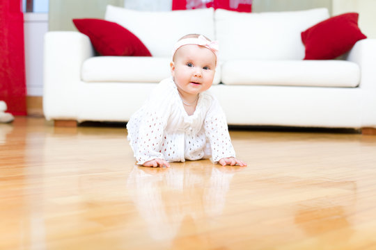 Happy eight month old baby girl crawling on a hardwood floor